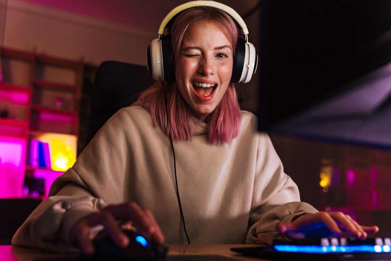 Junge Streamerin mit rosa Haaren lacht beim Zocken – perfekter Look dank laserhaarentfernung dauerhaft und schneller Beauty-Routine vor dem Stream