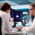 Zwei Ingenieure analysieren digitale Fertigungsdaten am Bildschirm, um mit einem APS System Produktionsablaeufe zu optimieren.