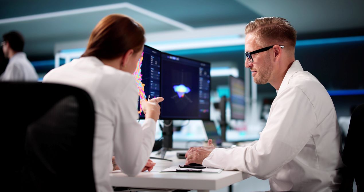 Zwei Ingenieure analysieren digitale Fertigungsdaten am Bildschirm, um mit einem APS System Produktionsablaeufe zu optimieren.