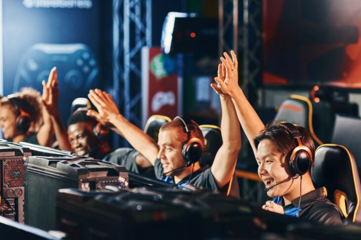 Erfolg feiern. Ein Team glücklicher professioneller E-Sport-Spieler gibt sich gegenseitig High-Fives, während sie an einem E-Sport-Turnier teilnehmen.